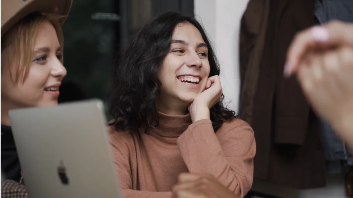 People talking beside a laptop with clothing hanging in the background