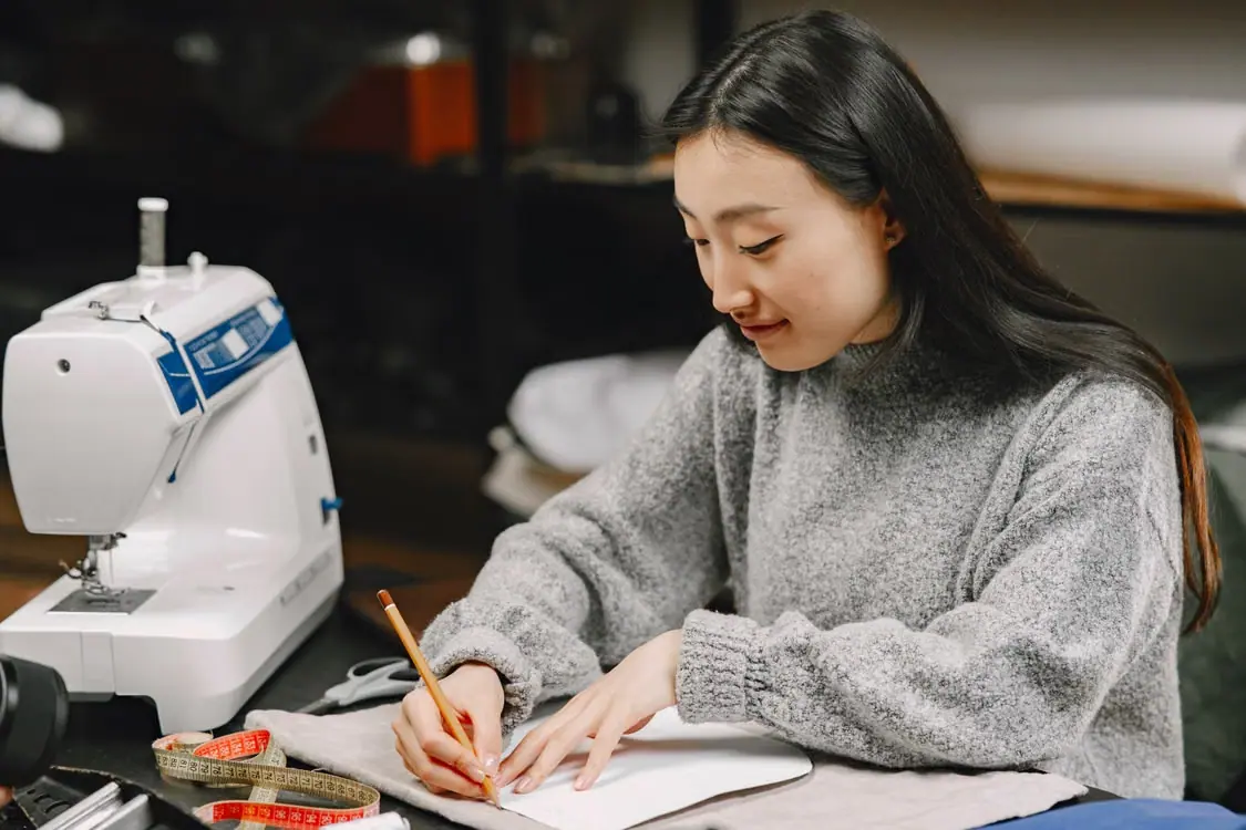 Apparel designer drafting a custom garment pattern beside a sewing machine and measuring tape