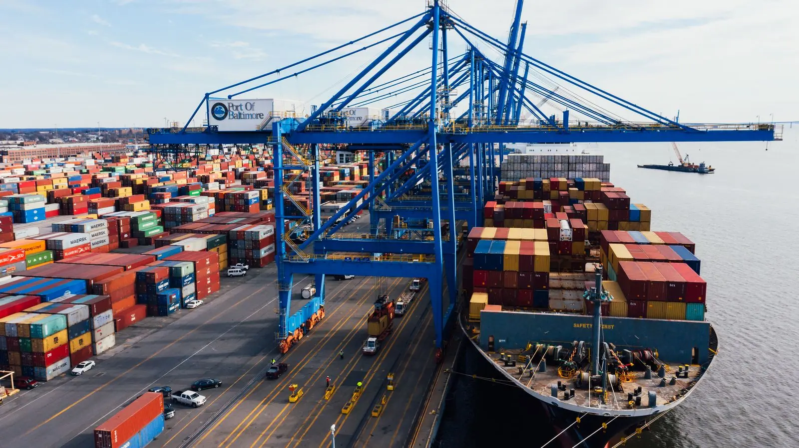 Representative cargo containers stacked at a port with cranes in the background